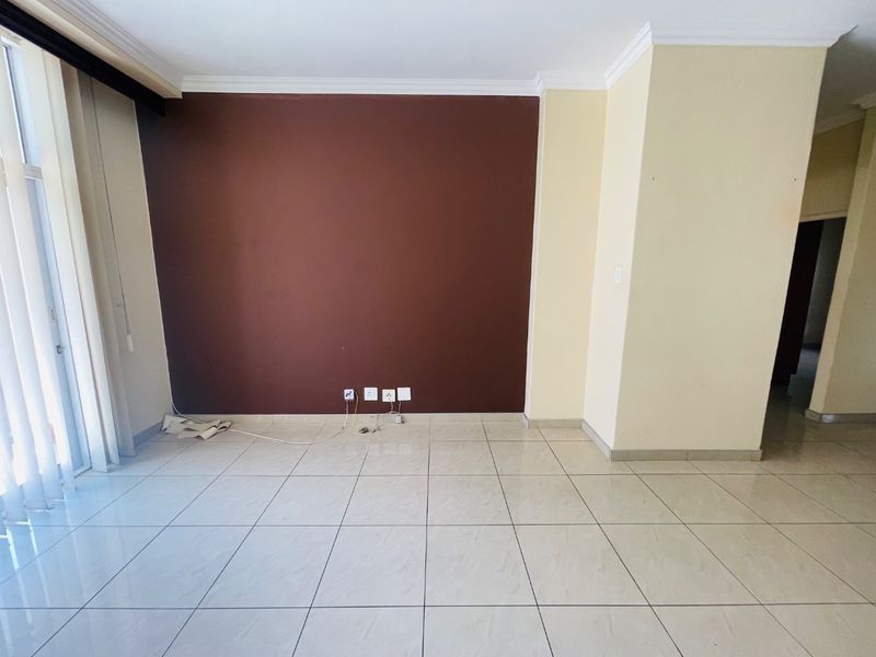 An empty living room featuring light-colored tiled flooring, crown molding, and a large sliding glass door providing natural light.