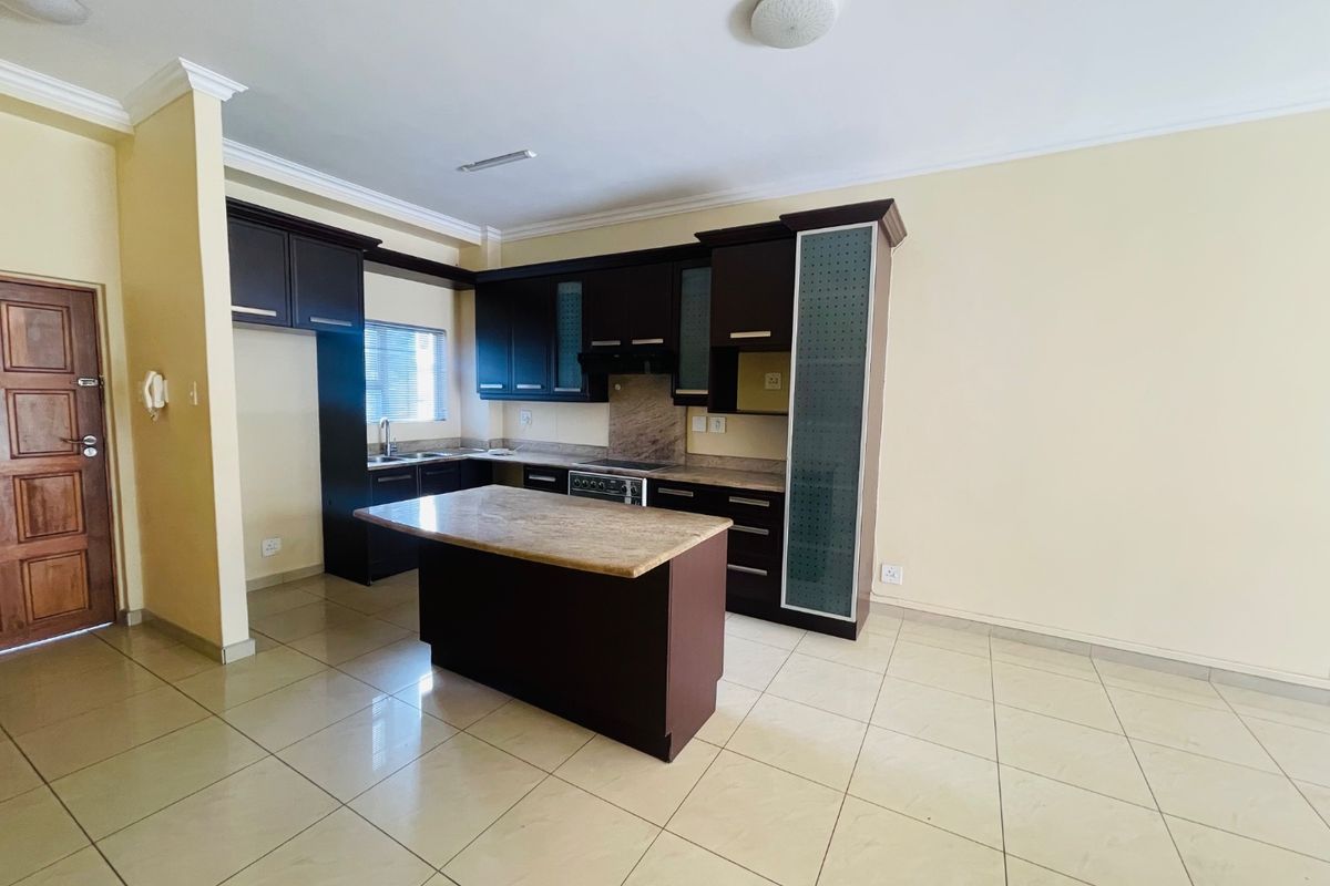 A spacious, empty kitchen featuring dark wood cabinetry, granite countertops, a central island, and neutral ceramic floor tiles.