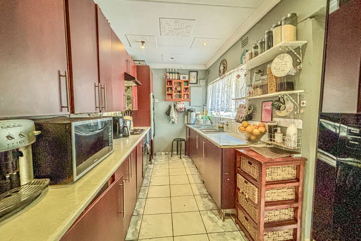 A functional galley-style kitchen featuring extensive built-in cabinetry, tiled flooring, and a stainless steel sink, offering a practical layout for daily meal preparation.