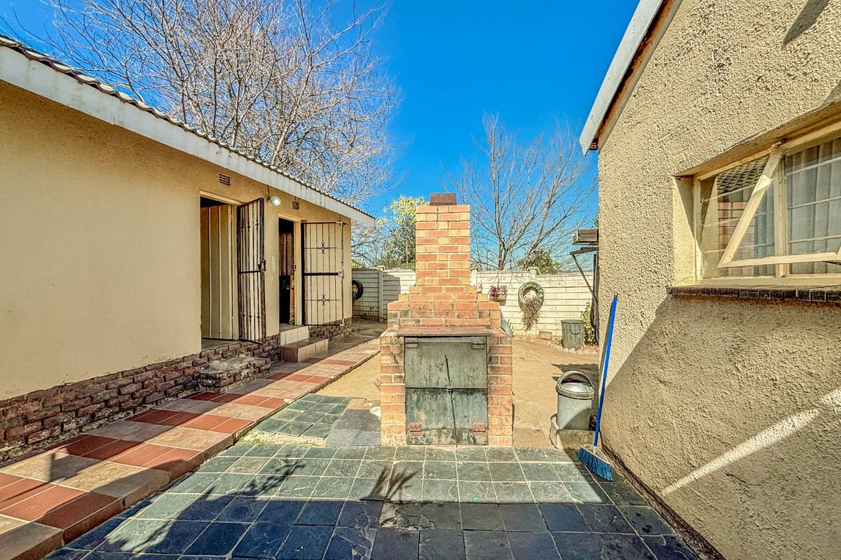 Rear courtyard area featuring a built-in brick braai, tiled patio flooring, and access to the main dwelling via security gates.