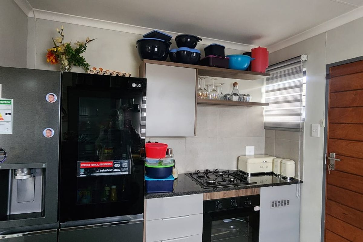 A compact kitchen area featuring modern fitted cabinetry, granite countertops, a built-in oven, and a gas hob, complemented by a roller blind.