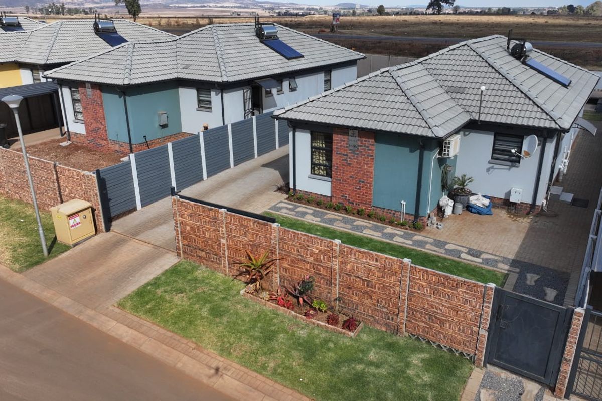 Aerial view of a residential property featuring tiled roofs with solar water heaters, paved driveways, and secure brick boundary walls.