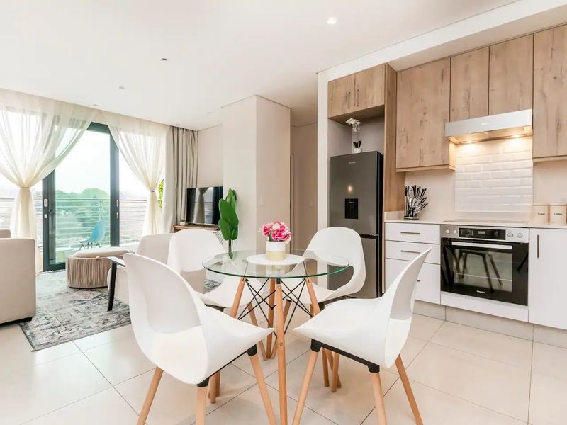 Modern open-plan apartment featuring a contemporary kitchen with light wood cabinetry, integrated appliances, and seamless flow to a bright living area with balcony access.