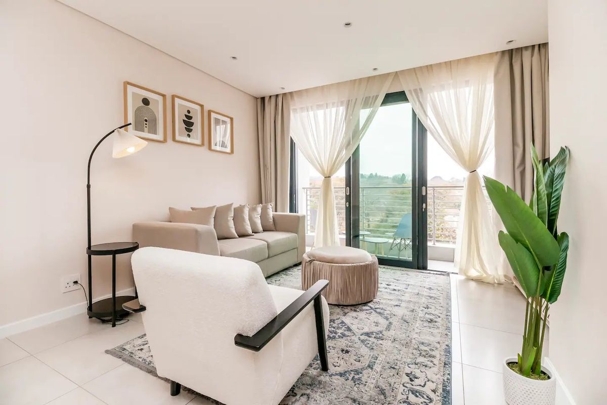 A bright and modern living room featuring tiled floors, recessed lighting, and large sliding glass doors that open onto a private balcony.