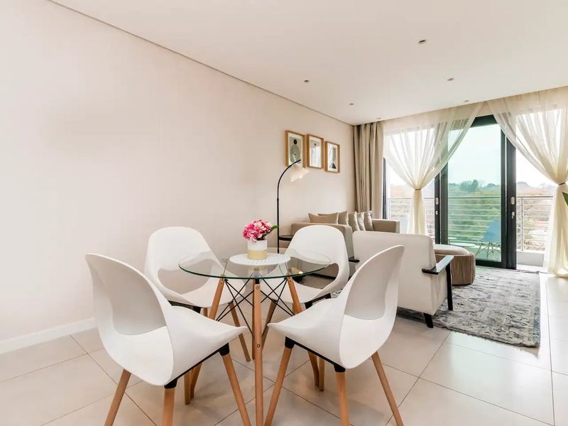 Bright open-plan living and dining area featuring neutral tiled flooring, recessed lighting, and large sliding glass doors leading to a private balcony.