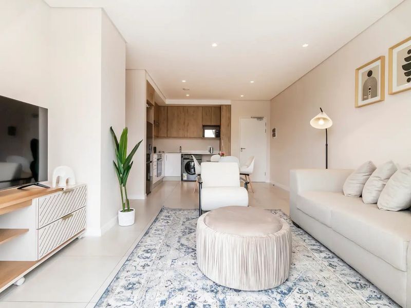 A modern open-plan living and kitchen area featuring neutral tones, recessed lighting, and sleek built-in cabinetry, creating a bright and cohesive living space.