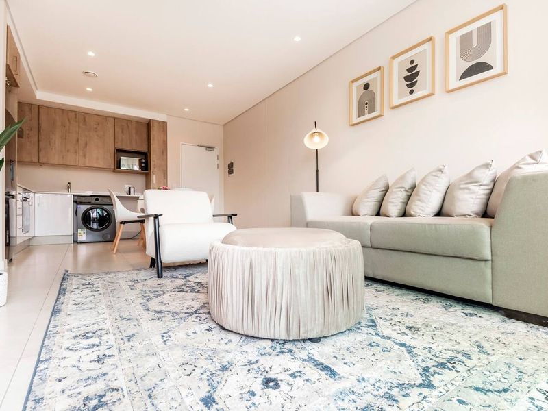 Modern open-plan living area featuring a sleek kitchen with built-in cabinetry and integrated appliances, seamlessly flowing into a bright and comfortable lounge space.