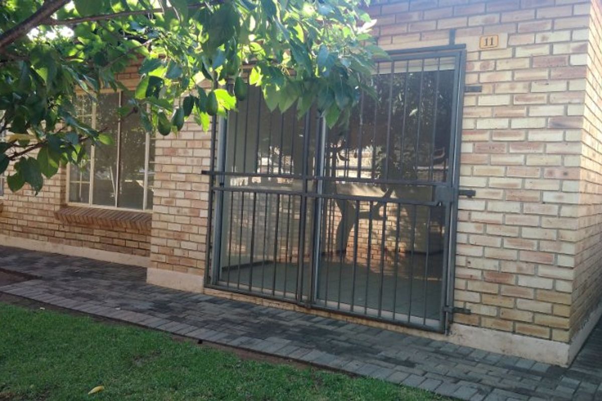 Rear exterior view of the property featuring a face brick facade, paved walkway, and a secure metal gate over the sliding door entrance.