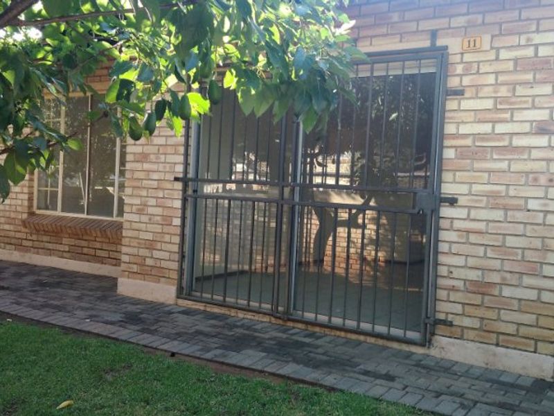 Rear exterior view of the property featuring a face brick facade, paved walkway, and a secure metal gate over the sliding door entrance.