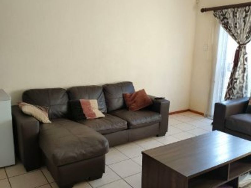 A living room featuring neutral tiled flooring and a sliding glass door providing access to the exterior.