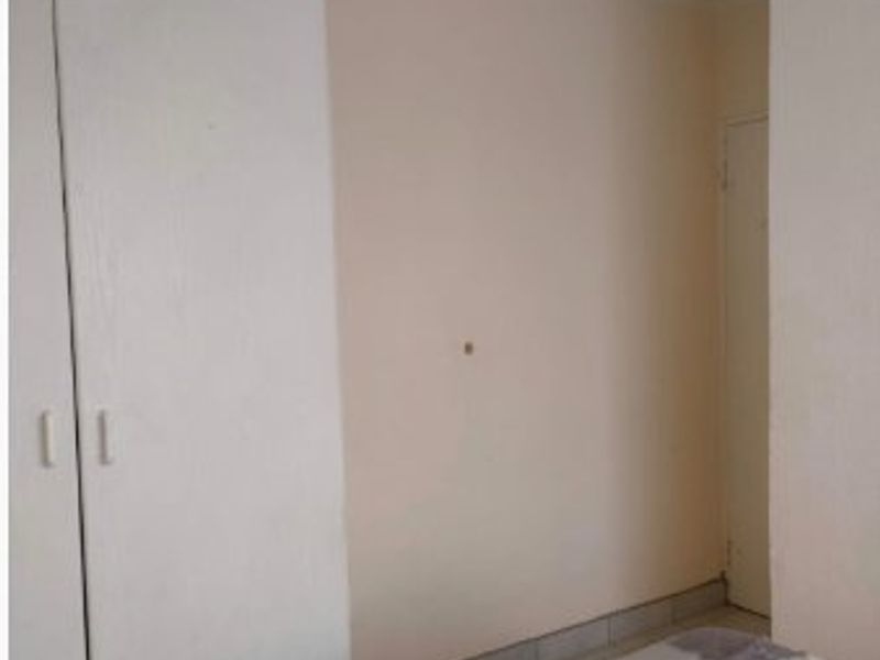 A bedroom interior featuring built-in cupboards and coving, showing signs of wear on the walls.