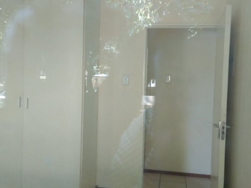 A vacant bedroom featuring built-in cupboards and tiled flooring, viewed through a reflective surface.