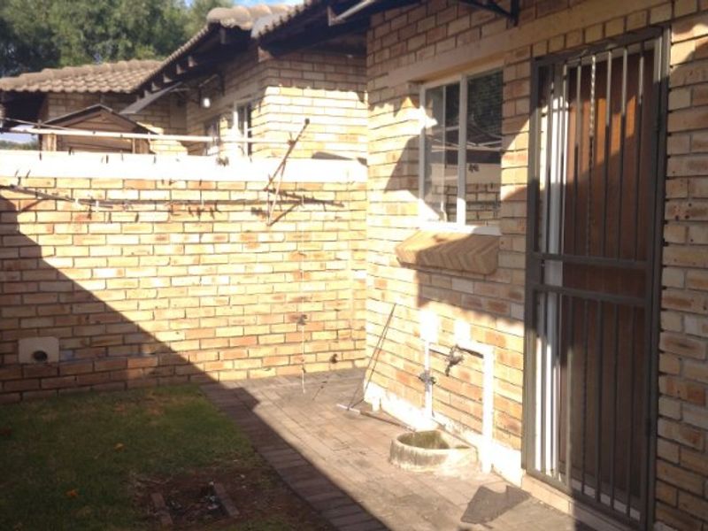 A rear exterior view of the property featuring face brick walls, a paved patio area, security gate, and external utility fixtures.
