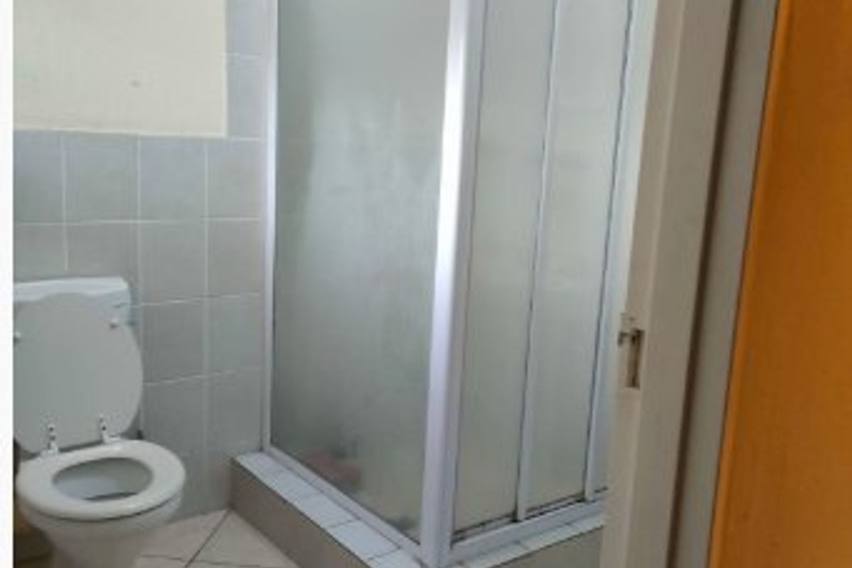 A functional bathroom featuring a corner shower enclosure, standard toilet, and tiled finishes throughout.