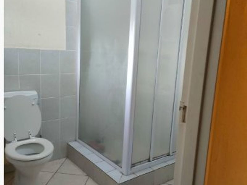 A functional bathroom featuring a corner shower enclosure, standard toilet, and tiled finishes throughout.