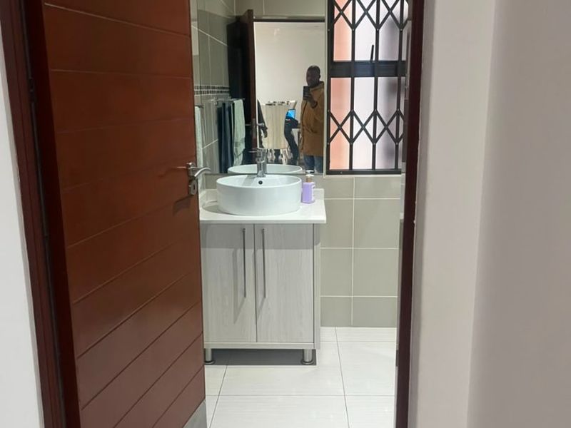 A modern bathroom featuring a vessel sink, vanity cabinet, and neutral wall and floor tiling.