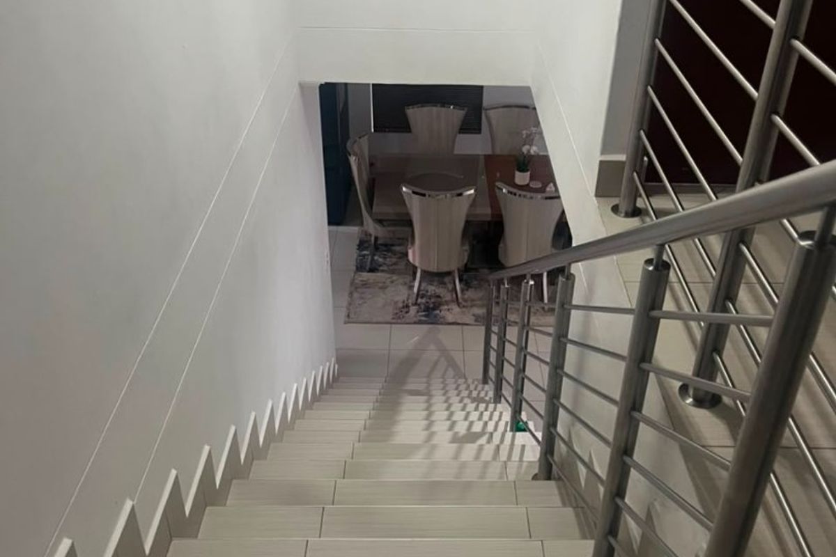 A view looking down a tiled staircase featuring a modern stainless steel balustrade, leading towards the lower level living area.