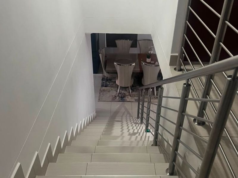 A view looking down a tiled staircase featuring a modern stainless steel balustrade, leading towards the lower level living area.