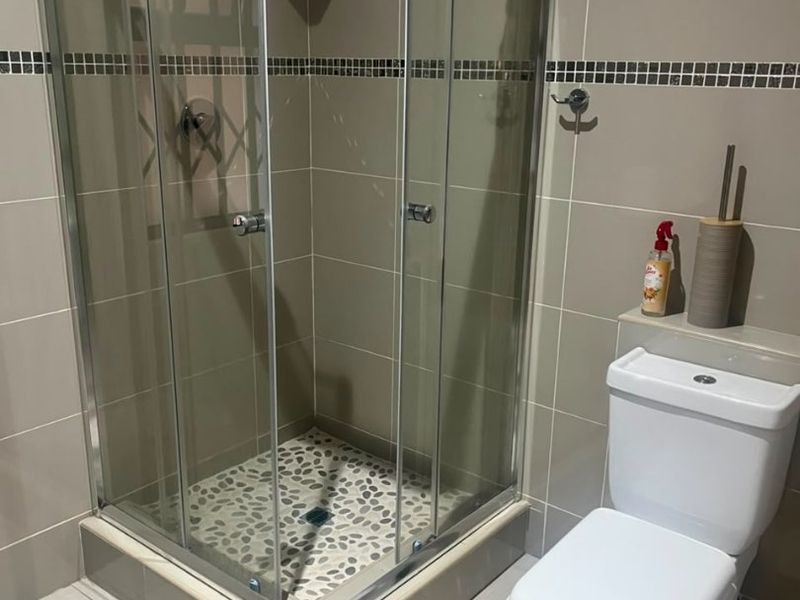 A modern bathroom featuring a glass-enclosed shower with pebble flooring and neutral ceramic wall tiles, complemented by a standard dual-flush toilet.