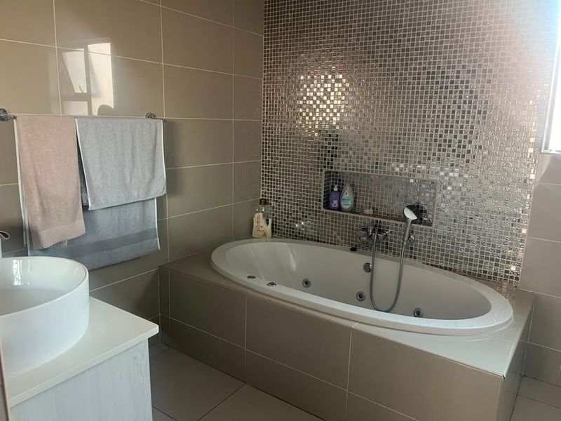 Modern bathroom featuring a built-in jetted bathtub, a striking mosaic tile feature wall with a recessed niche, and a contemporary vessel sink.