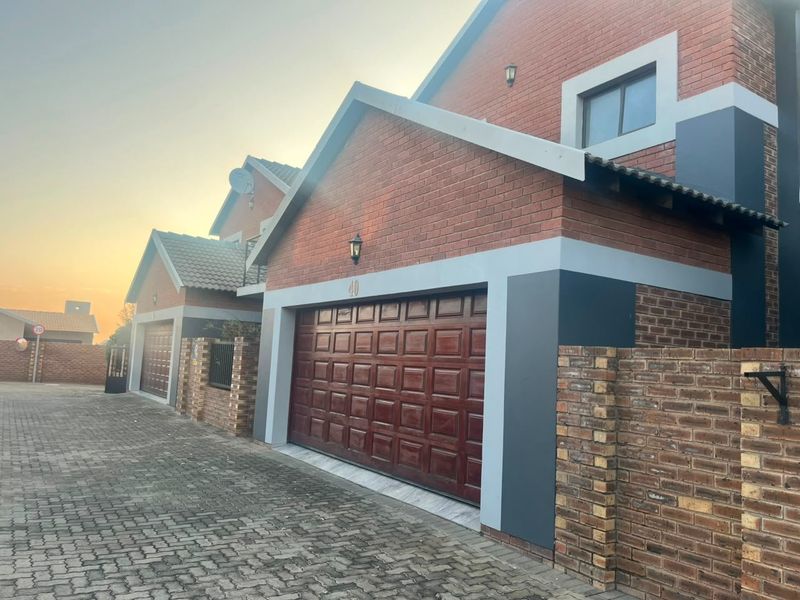 Front exterior view of a townhouse featuring a brick facade, paved driveway, and a secure sectional garage door.
