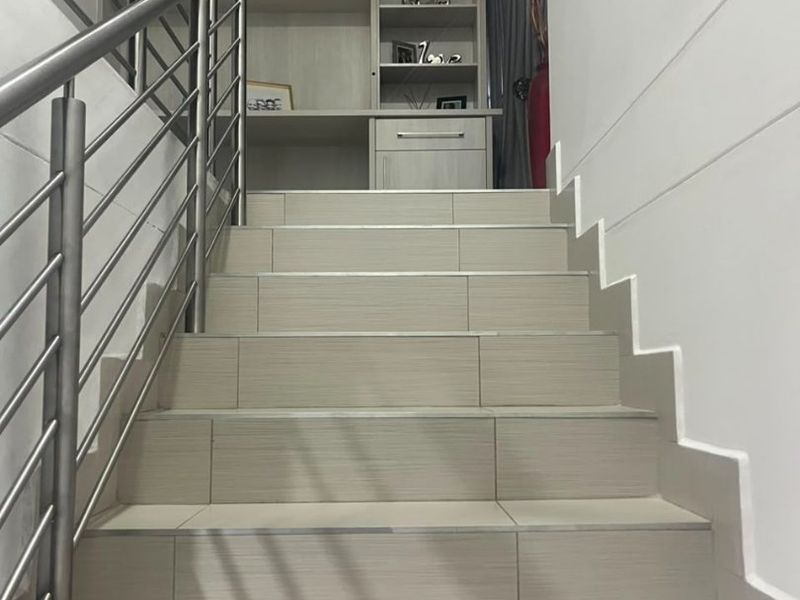A modern staircase featuring tiled steps, a sleek stainless steel balustrade, and a built-in shelving unit at the landing.
