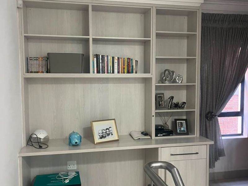 A functional home office area featuring custom built-in desk and shelving cabinetry, complemented by neutral tiled flooring and modern downlighting.