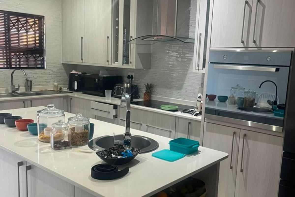 Modern kitchen featuring a central island, built-in oven, extractor fan, and ample cabinetry with a tiled backsplash and sleek finishes.