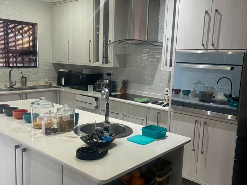 Modern kitchen featuring a central island, built-in oven, extractor fan, and ample cabinetry with a tiled backsplash and sleek finishes.