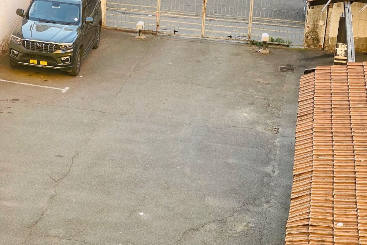 An elevated view of a paved rear parking area featuring a metal security gate and weathered perimeter walls.