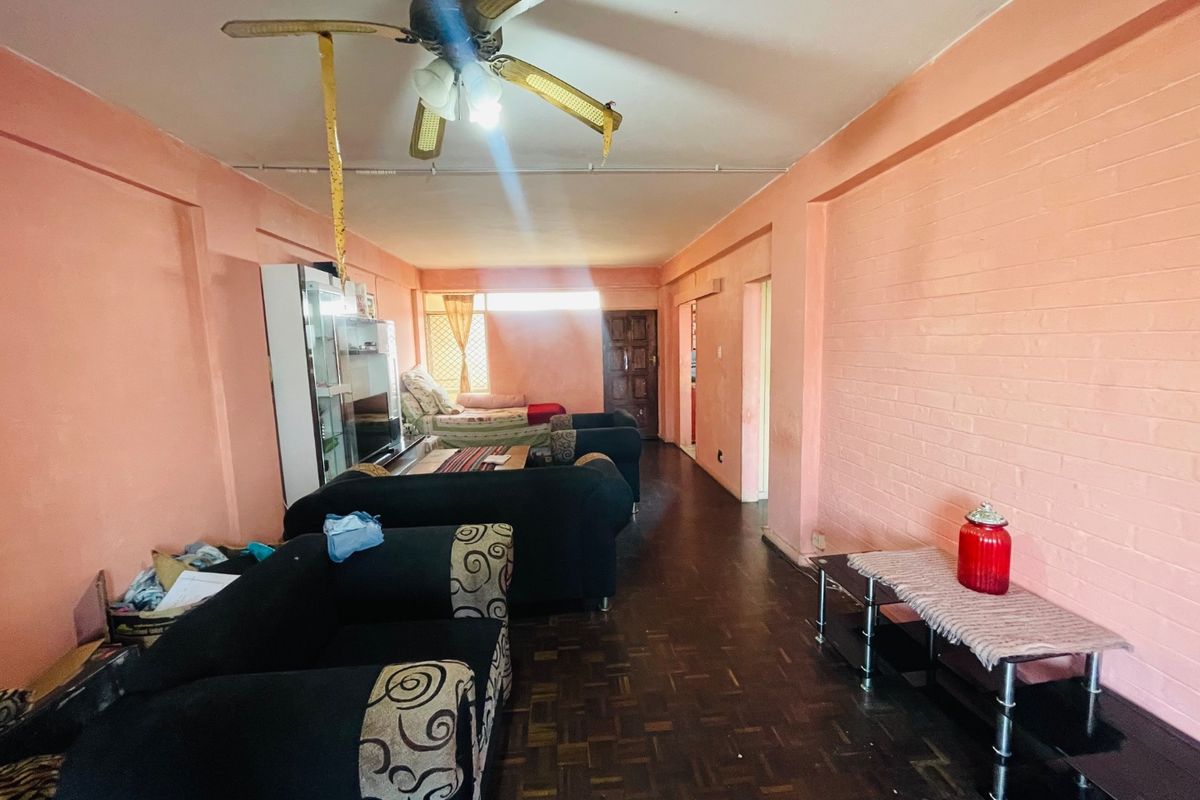 Spacious living area featuring parquet flooring, an exposed brick wall, and a ceiling fan, offering a blank canvas for modernization and interior updates.