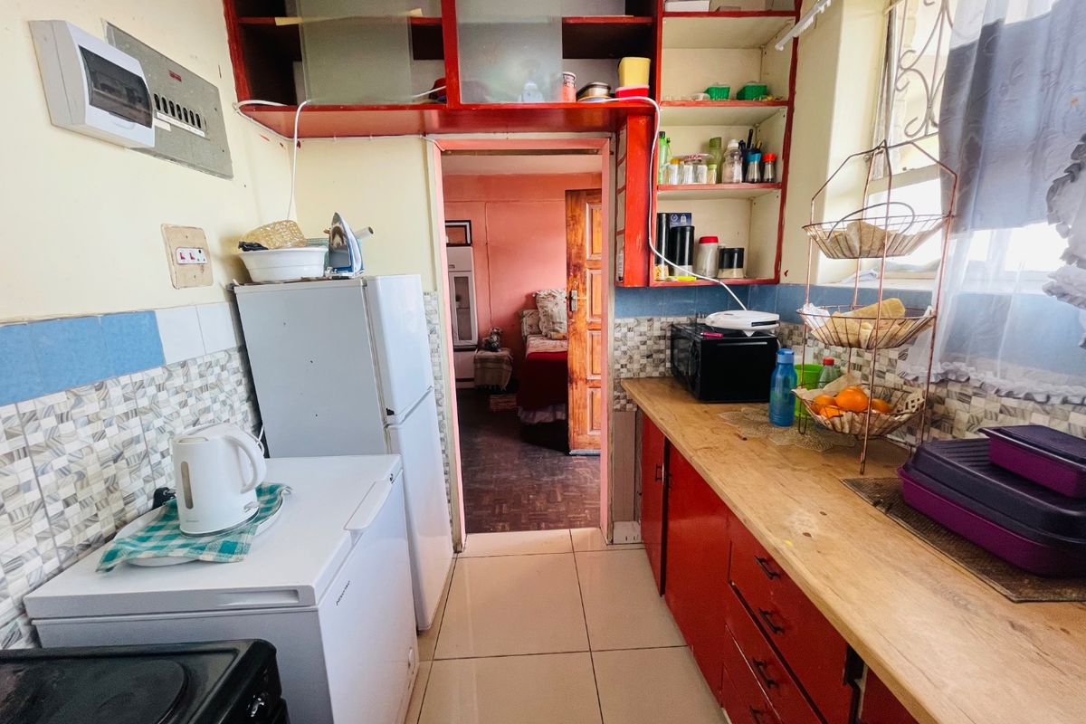 A compact kitchen featuring built-in red cabinetry, tiled splashbacks, and tiled flooring, providing a functional workspace with direct access to the adjacent room.