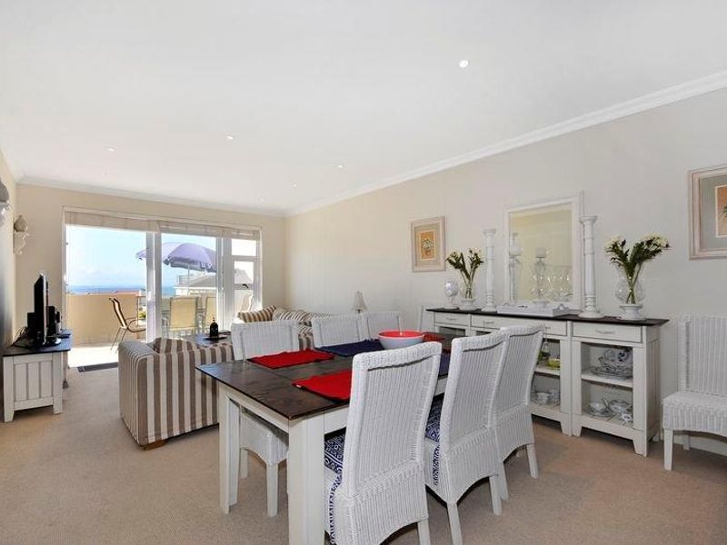 Spacious open-plan living and dining area featuring neutral carpeting, recessed lighting, and large sliding doors leading to a private balcony with ocean views.