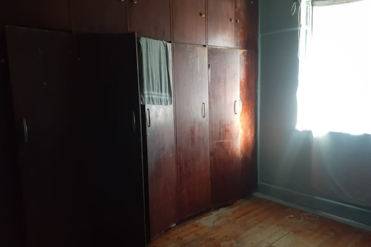 A bedroom featuring original timber flooring and extensive built-in wooden cabinetry, offering ample storage space in a dated but functional setting.