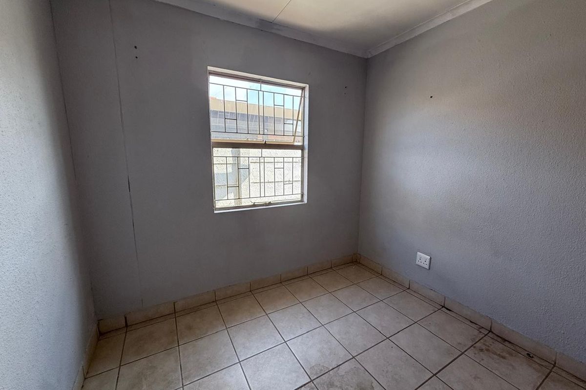 An empty bedroom featuring tiled flooring, a window with security bars, and neutral wall finishes, ready for personalization.