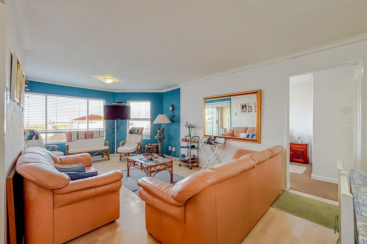 A bright living room featuring laminate flooring, large windows with venetian blinds, and a feature wall, providing a comfortable and functional living space.