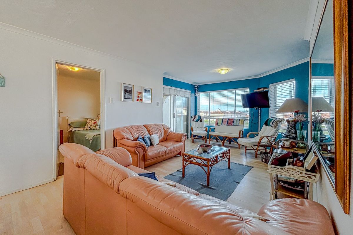 Spacious living room featuring laminate flooring, large windows with venetian blinds, and direct access to a balcony through sliding glass doors.
