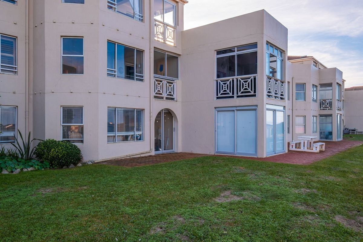 Rear view of the apartment building featuring a paved patio area, lawn, and access to ground floor units via sliding glass doors.