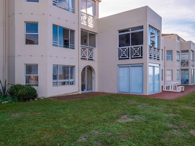 Rear view of the apartment building featuring a paved patio area, lawn, and access to ground floor units via sliding glass doors.