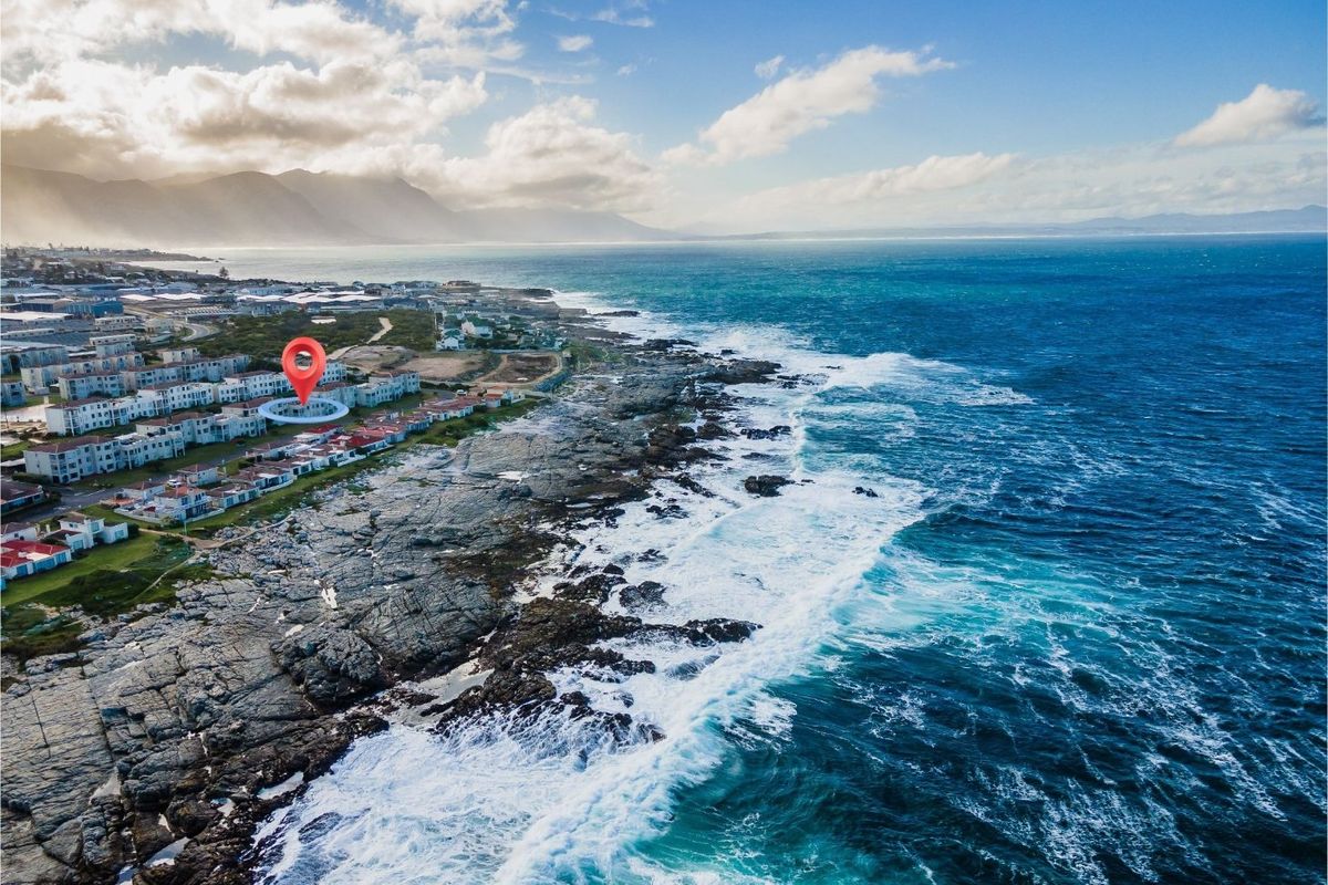 An aerial view of a coastal residential apartment complex situated along the rocky shoreline with ocean views.