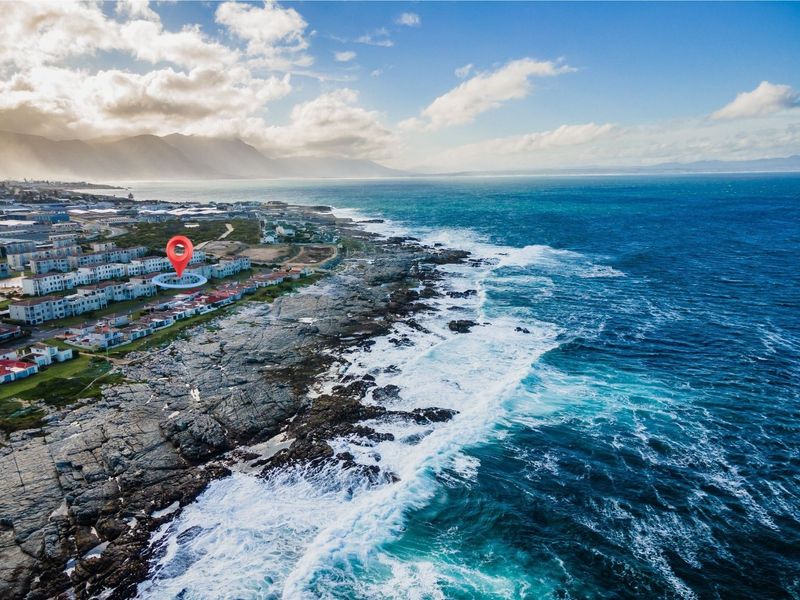 An aerial view of a coastal residential apartment complex situated along the rocky shoreline with ocean views.