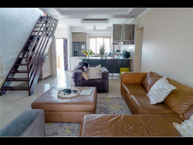 Open-plan living area featuring a modern kitchen with island, tiled flooring, and a prominent wooden staircase leading to the upper level.