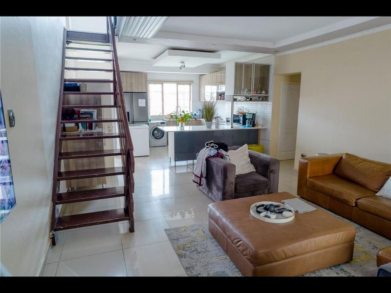 Open-plan living area featuring a modern kitchen with island, tiled flooring, and a prominent staircase leading to the upper level.