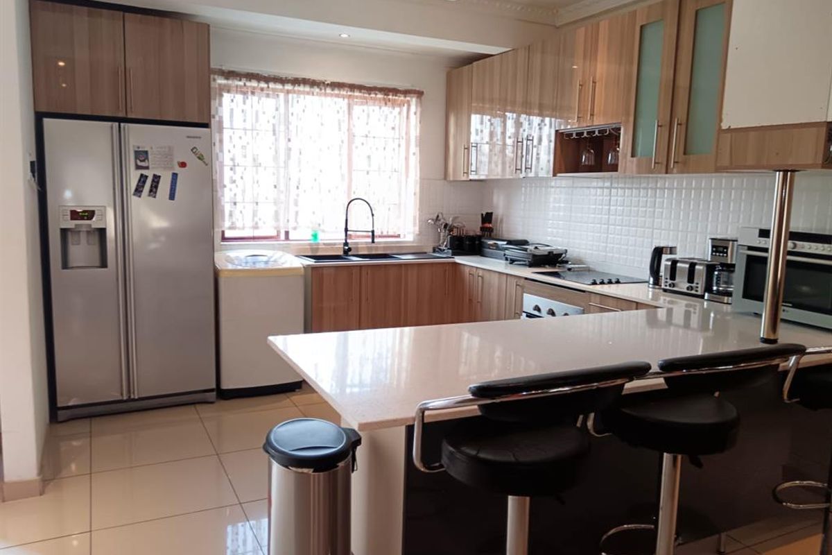 A functional kitchen featuring wood-finish cabinetry, stone countertops, a central island with breakfast bar seating, and integrated appliances.