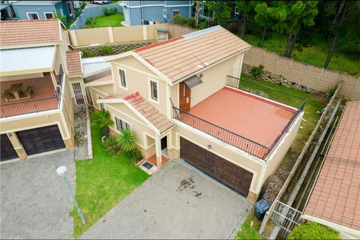 Aerial view of a residential property featuring a double garage, paved driveway, and an upper-level balcony with metal railings.