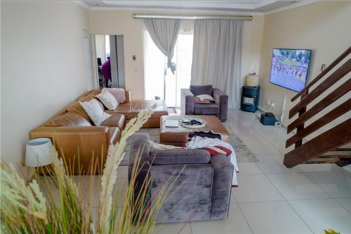 A spacious living room featuring tiled flooring, a wooden staircase, and sliding glass doors that provide access to the exterior.