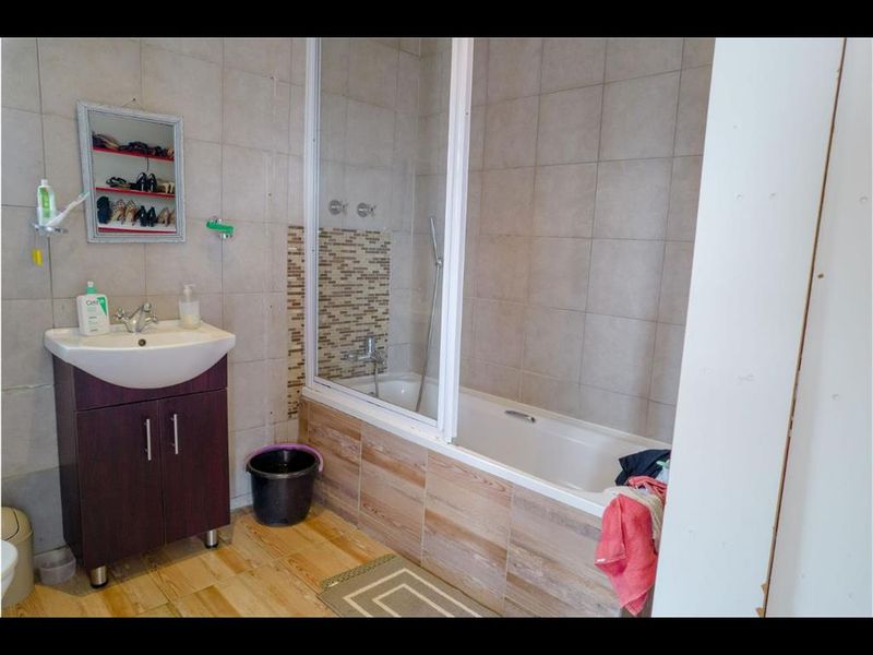 A functional bathroom featuring a vanity cabinet with basin, a bathtub with integrated shower screen, and neutral wall and floor tiling.