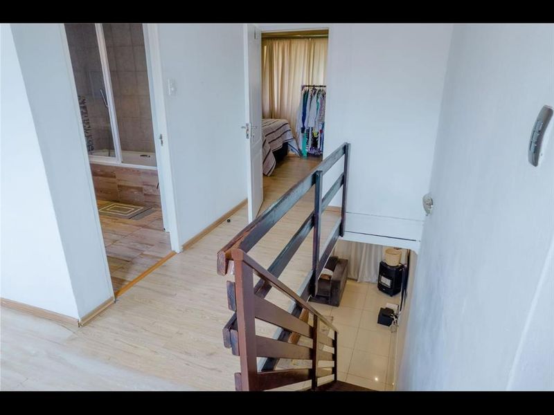 Upper level hallway featuring laminate flooring and a timber staircase with balustrade, providing access to the bathroom and bedroom areas.