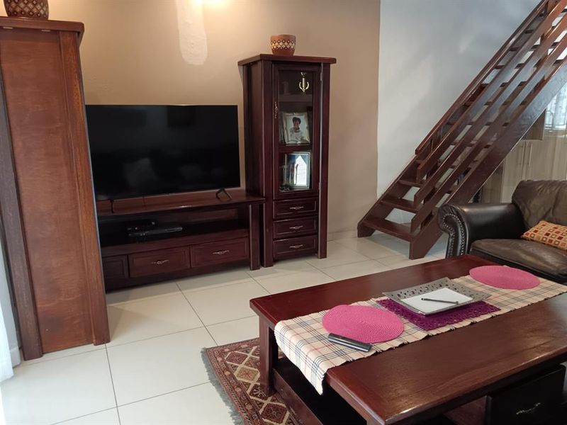 A living room featuring tiled flooring and a wooden staircase, with neutral wall tones and visible areas requiring paint touch-ups.
