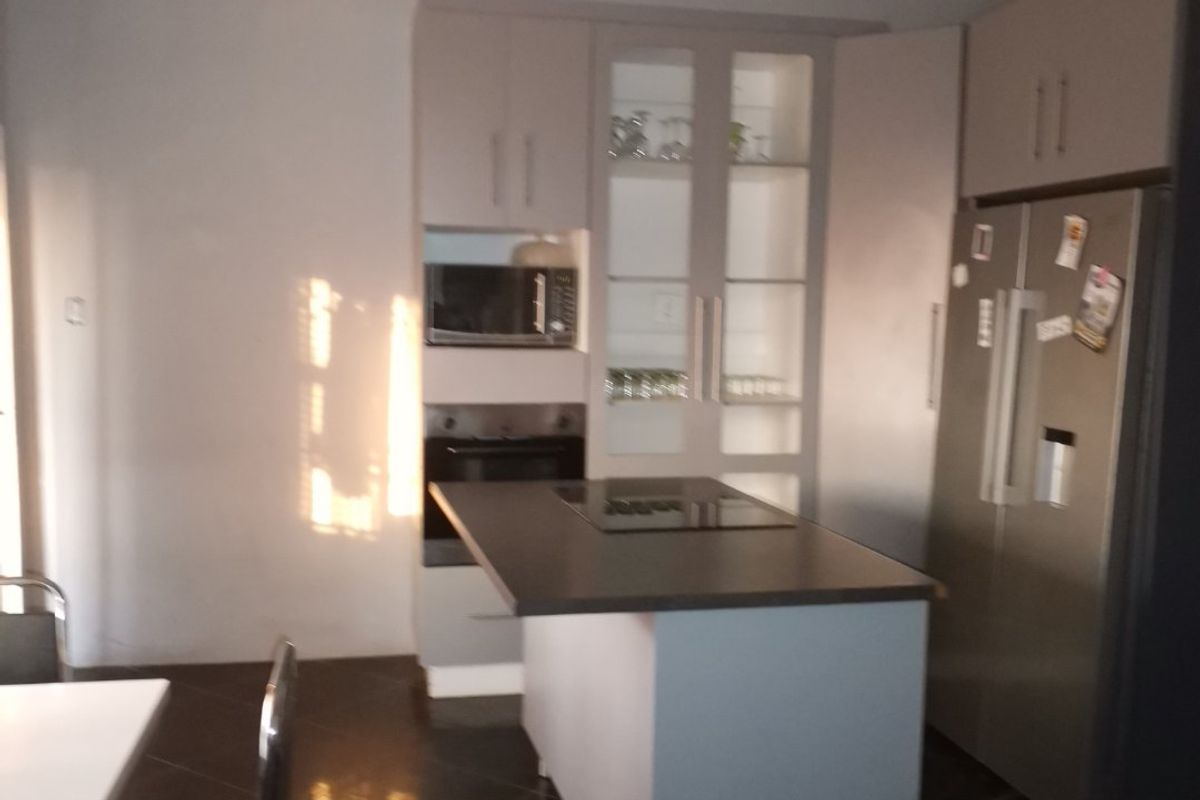 Modern kitchen featuring a central island, built-in oven, microwave, and sleek cabinetry with glass display units, complemented by dark tiled flooring and a decorative ceiling.